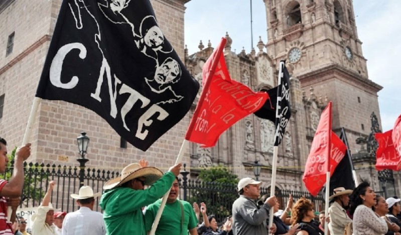 Grupo de maestros de la CNTE con banderas rojas y negras levantadas delante de Catedral de Morelia, Michoacán durante manifestaciones y protestas