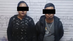 Se observa a un hombre y una mujer parados, con cintilla negra en ojos.