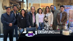 Se observa a hombres y mujeres que están sonriendo y parados, hay pasteles y micrófonos.