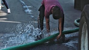 Persona sujetando una manguera con una fuga de agua potable.