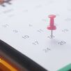 Un calendario sobre una mesa, marcado en la casilla de una fecha con un tachuela de color rosa