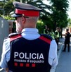 Policía miembro de los Mossos d'Esquadra visto de espaldas volteando hacia la izquierda con otros oficiales y una ambulancia vistos desenfocados en el fondo