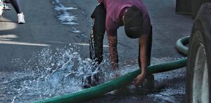 Persona sujetando una manguera con una fuga de agua potable.