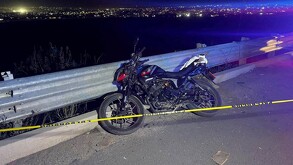 Motocicleta color negro estacionada al lado de un muro de contención al borde de un barranco con una cinta policiaca acordonando el stio