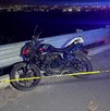 Motocicleta color negro estacionada al lado de un muro de contención al borde de un barranco con una cinta policiaca acordonando el stio