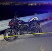 Motocicleta color negro estacionada al lado de un muro de contención al borde de un barranco con una cinta policiaca acordonando el stio