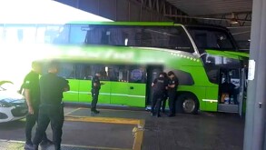 Camión de transporte público color verde estacionado dentro de una central camionera con policías alrededor