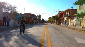 Vialidades en Santa Cruz de las Flores en Tlajomulco con un niño paseando en bicicleta y personas caminando en la banqueta con casas alrededor