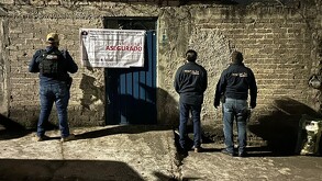 Tres agentes de la Fiscalía del Estado de Michoacán frente al exterior de un inmueble con una puerta azul metálica con letreo de aseguramiento