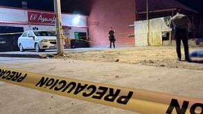 Se observa una calle, hay una persona parada, un cuerpo tendido en el suelo, una cinta amarilla de precaución.