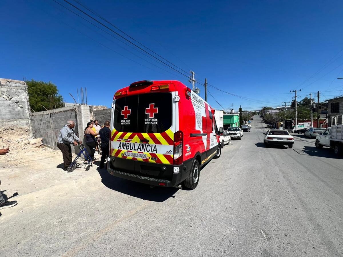 Una ambulancia de la Cruz Roja se encuentra estacionada en una calle mientras paramédicos atienden un reporte y vecinos observan la escena.