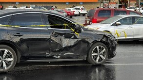 Auto BYD color negro con la puerta derecha aboyada por un choque y con una cinta policiaca encima acordonando la escena en un estacionamiento