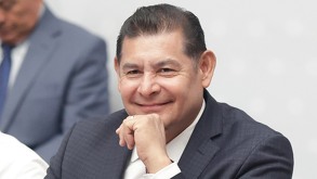 Hombre vestido de traje sonríe mientras tiene el puño en el rostro.