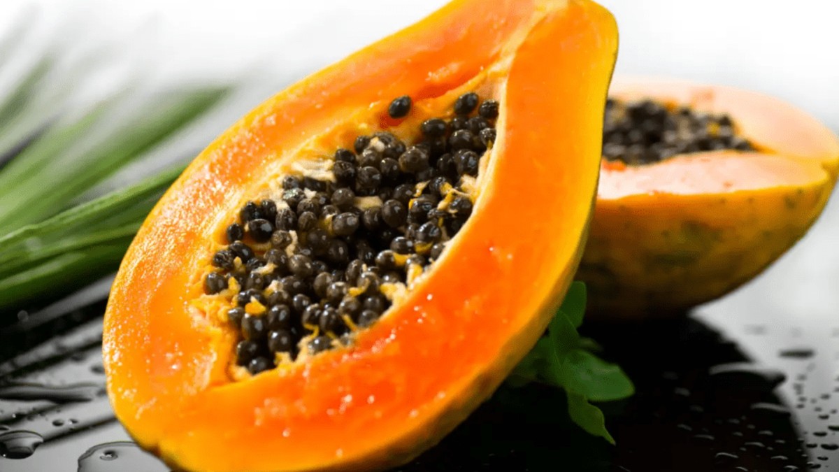 Papaya partida por la mitad con las semillas expuestas colocada sobre una mesa con hojas verdes detrás