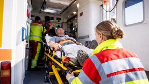 Paramédicos suben a un paciente en camilla a una ambulancia mientras preparan el equipo para su traslado de emergencia.