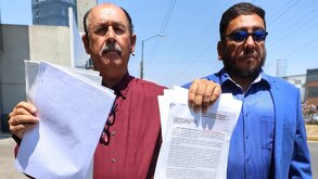 Dos hombres sostienen documentos en la mano correspondientes al fallo de un juicio.