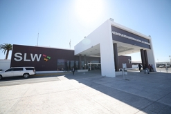 Personas caminan con maletas hacia la entrada del Aeropuerto Internacional de Saltillo, donde se observan las instalaciones principales.