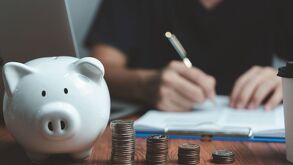 Una alcancía sobre un mesa con varias columnas de monedas apiladas