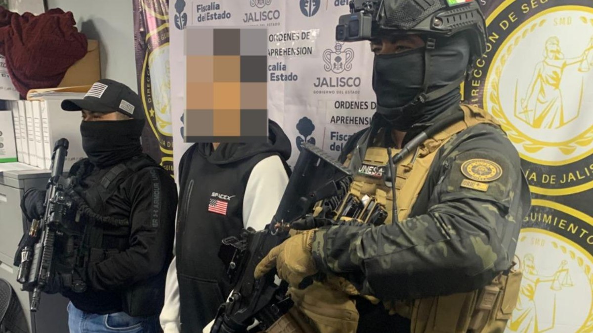 Dos oficiales de la Fiscalía de Jalisco a los costados de un hombre detenido y con la cara censurada