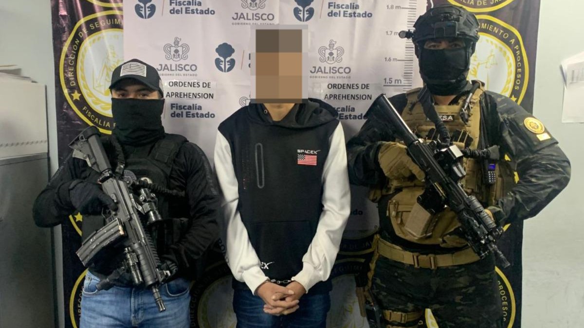 Hombre detenido con la cara censurada en medio de dos oficiales de la Fiscalía de Jalisco portando armas largas