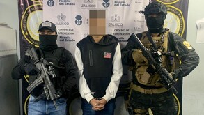 Hombre detenido con la cara censurada en medio de dos oficiales de la Fiscalía de Jalisco portando armas largas