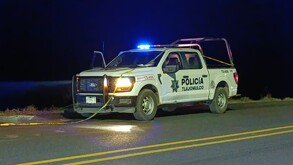 Patrulla de la Policía Municipal de Tlajomulco estacionada a un costado de un tramo carretero con una cinta policiaca encima durante la noche