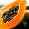 Papaya partida por la mitad con las semillas expuestas colocada sobre una mesa con hojas verdes detrás