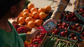 Dos personas usando el método de pago Tap To Pay en un puesto de verduras mientras usan un celular como terminal de pago