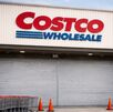 Entrada de una tienda Costco con la cortina metálica abajo, carritos alineados al costado y conos naranjas frente al acceso principal.
