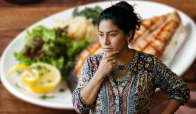 Mujer mexicana adulta pensando qué hacer de comer con un platillo de fondo fuera de foco.