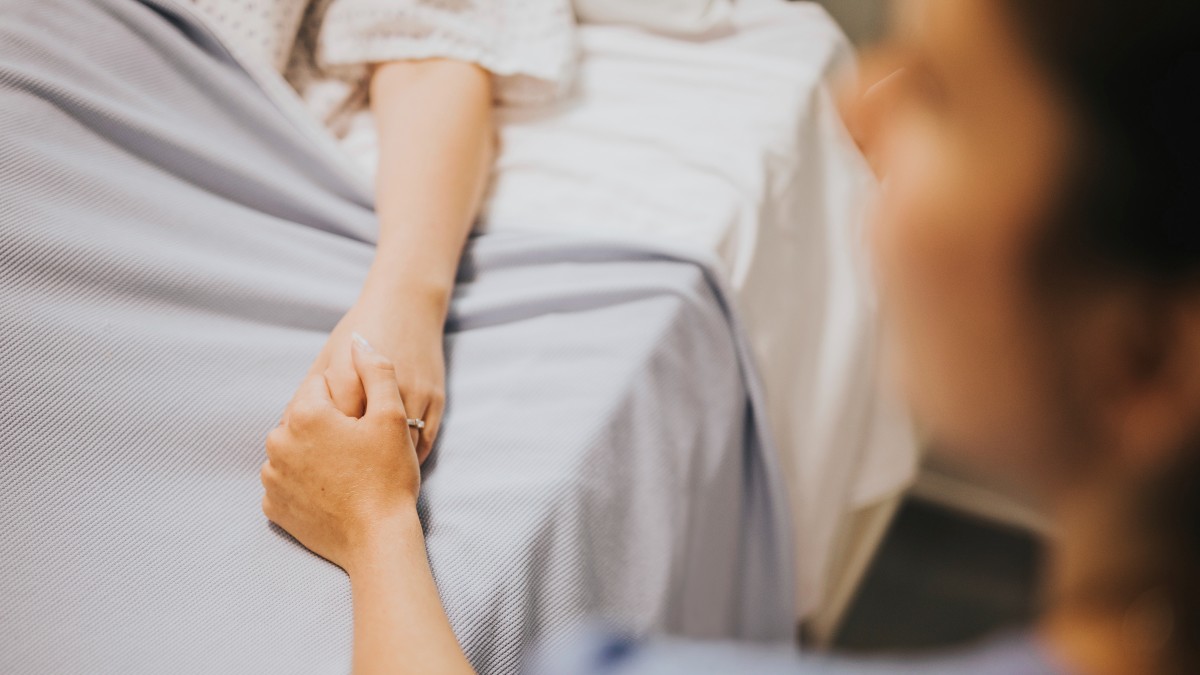 Persona tomando la mano de un paciente en un hospital