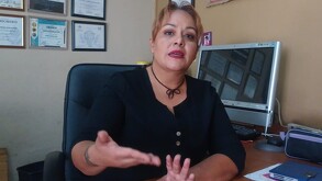 Se observa a una mujer hablando, está sentada, viste una playera color negro.