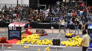Imagen de la competencia de First Robotics donde vemos unos de los robots en acción en la cancha de competencia. Al fondo se muestran las gradas con público