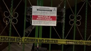 Reja de una vivienda con aviso oficial de “inmueble asegurado” colocado por autoridades, junto a cinta amarilla de escena del crimen que restringe el acceso.