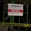 Reja de una vivienda con aviso oficial de “inmueble asegurado” colocado por autoridades, junto a cinta amarilla de escena del crimen que restringe el acceso.