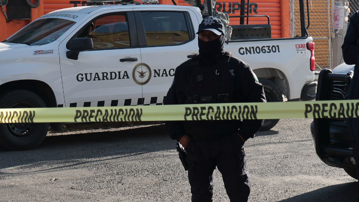 Policía con el rostro cubierto parado detrás de una cinta de seguridad.
