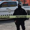Policía con el rostro cubierto parado detrás de una cinta de seguridad.