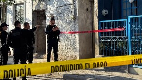 Oficiales de la Policía de Zapopan delante de una casa con portón azul acordonada con cintas policiacas