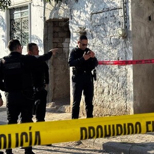 Oficiales de la Policía de Zapopan delante de una casa con portón azul acordonada con cintas policiacas
