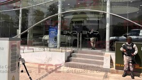 Vista del exterior de una agencia automotriz BYD en Colima con un militar sosteniendo una arma larga al lado de las escaleras