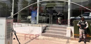 Vista del exterior de una agencia automotriz BYD en Colima con un militar sosteniendo una arma larga al lado de las escaleras