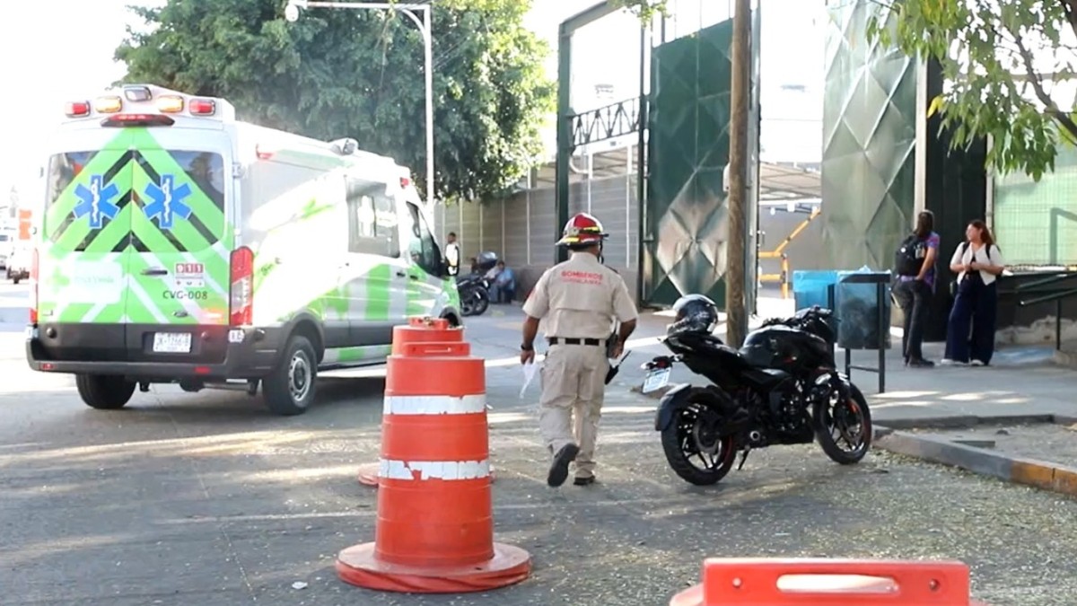 Oficial de Protección Civil y Bomberos de Guadalajara afuera de una empresa con una ambulancia de la Cruz Verde y una moto al lado, y conos naranjas alrededor