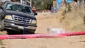 Se observa una camioneta, una cinta roja de precaución y un cuerpo tendido en el piso arriba de éste hay una manta blanca.