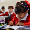 Niña escribiendo en un cuaderno dentro de un salón de clases en Jalisco con otros alumnos desenfocados en el fondo