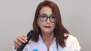 Mujer de lentes y camisa blanca sosteniendo un micrófono.