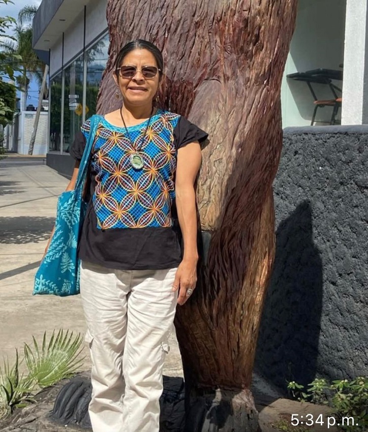 Mujer con gafas y vestidura mixe parada junto a un árbol.