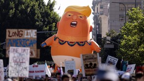 Inflable de Donald Trump caricaturizado como un bebé en medio de una multitud de manifestantes con letreros durante protestas en EU