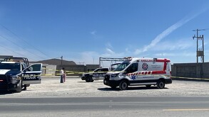 Se observa un terreno en donde están estacinadas una ambulancia y otra camioneta, hay una cintilla roja de precaución.