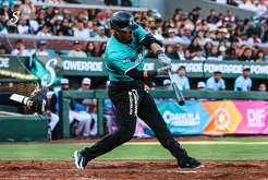 ugador de los Saraperos de Saltillo realiza un swing durante un partido, con uniforme verde y negro, en un estadio lleno de aficionados; al fondo se aprecia el