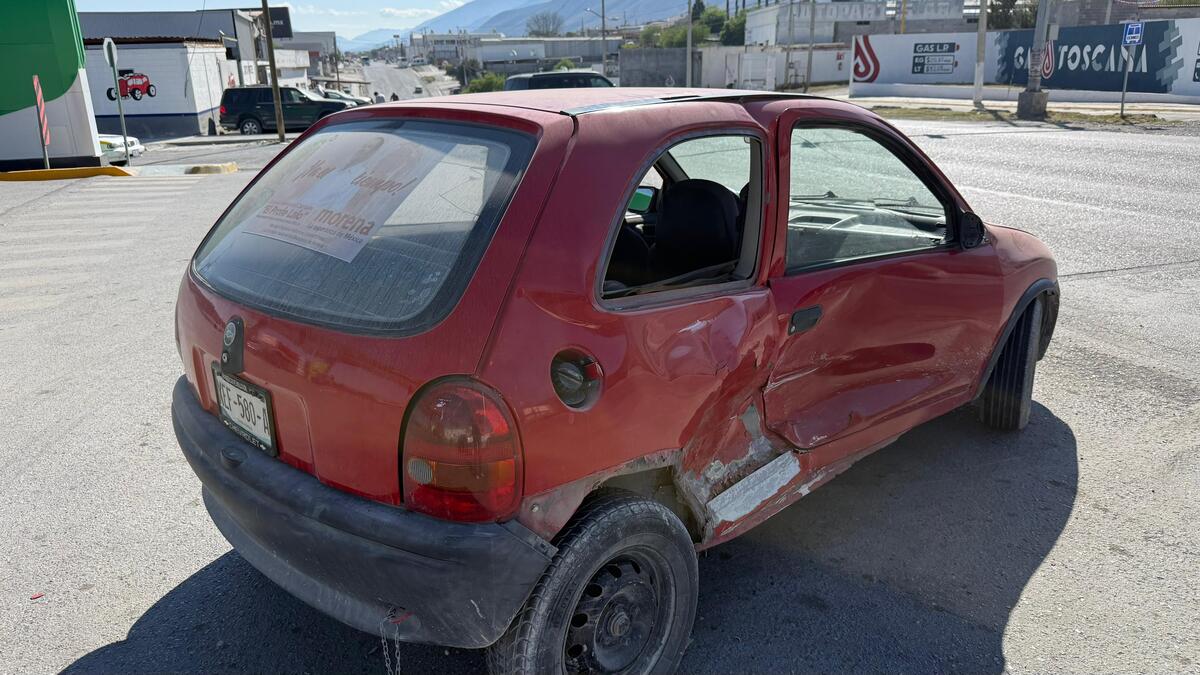 Un automóvil compacto rojo presenta daños visibles en la parte lateral tras un accidente, mientras permanece detenido en una vialidad amplia con construcciones
